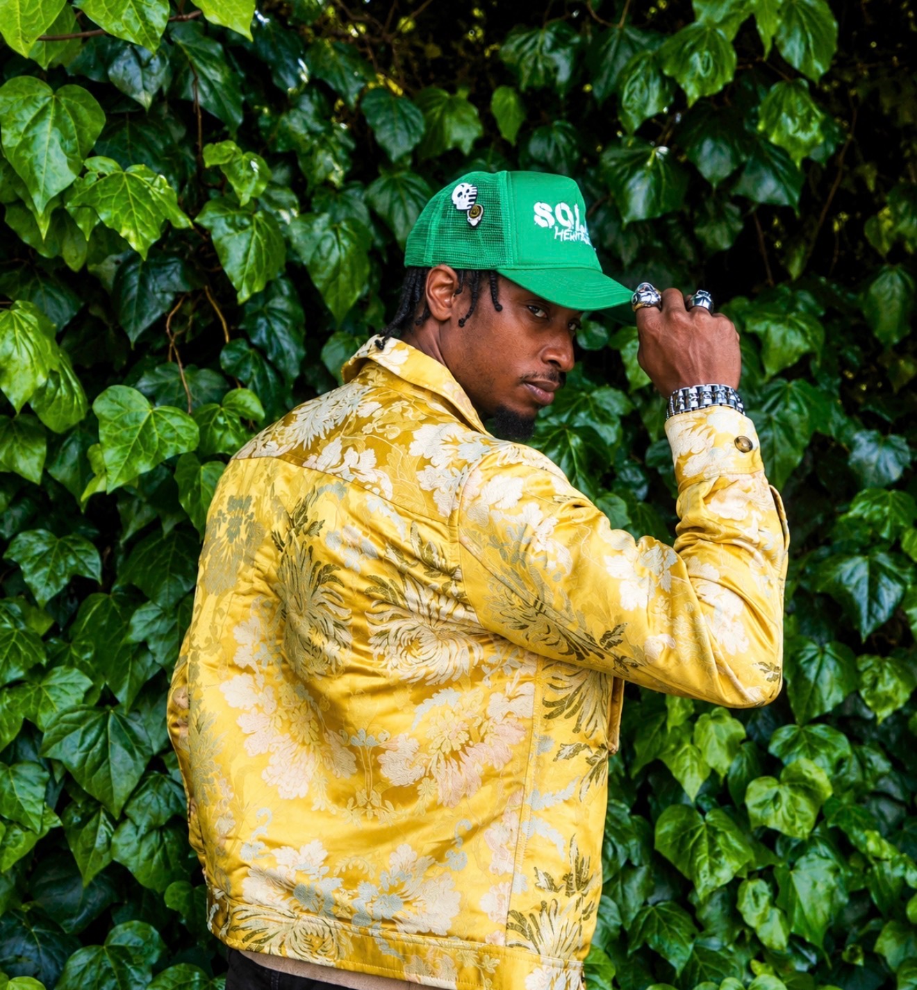 Who Is Lantern in a yellow jacket and green cap against greenery